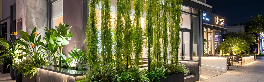 Aménagement végétal extérieur avec grands bacs noirs et plantes artificielles suspendues à l'entrée d'un restaurant à Marrakech.