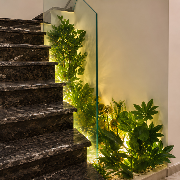 Création d’un jardin végétal intégré sous un escalier avec galets décoratifs et éclairage.