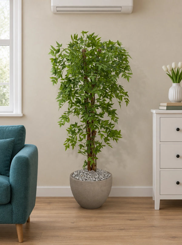 Arbre artificiel Nandina au feuillage vert dense disposé dans un salon moderne à côté d'un canapé bleu et d'une commode blanche