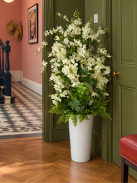 Composition de fleurs artificielles blanches et jasmins en vase haut disposée dans le coin d'un hall d'entrée élégant.