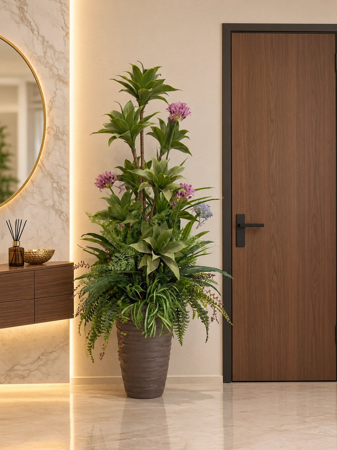 Grande composition florale artificielle avec agapanthes mauves et feuillages denses posée dans l'entrée d'une maison près d'une console et d'un miroir doré.
