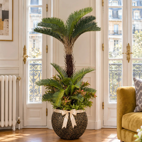 Palmier cycas artificiel effet réel dans un grand pot doré effet pierre, à côté d'un canapé moutarde dans un salon moderne de villa