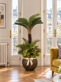 Palmier cycas artificiel effet réel dans un grand pot doré effet pierre, à côté d'un canapé moutarde dans un salon moderne de villa