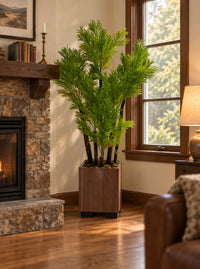 Plante artificielle Podocarpus du Japon hauteur 145 cm et largeur 70 cm mise en valeur dans un coin salon près d'une cheminée en pierre et fenêtre en bois