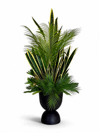 Vue studio de la composition végétale artificielle Sansevieria et palmiers montée dans son vase noir mat incassable au design sculptural.   